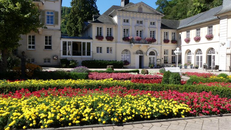 Ein schöner Garten mit bunten Blumenbeeten um ein elegantes Gebäude. Die Umgebung ist grün und einladend.