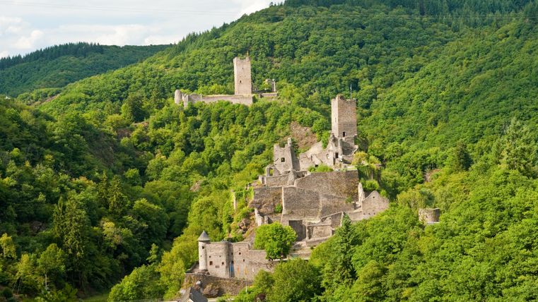 Eine beeindruckende Burgruine, umgeben von einer grünen Landschaft. Im Hintergrund sind weitere Turmreste sichtbar.