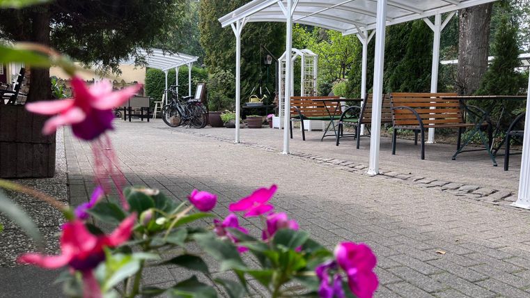 Ein einladender Außenbereich mit Sitzgelegenheiten und gedeckten Tischen. Bunte Blumen im Vordergrund verleihen dem Ort eine fröhliche Atmosphäre.