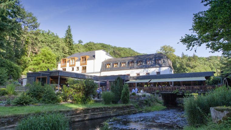 Ein charmantes Restaurant inmitten grüner Natur. Das Gebäude ist modern und bietet eine Terrasse mit Blick auf einen kleinen Fluss.