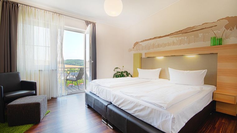 Ein modernes Hotelzimmer mit zwei Einzelbetten und hellen Vorhängen. Der Raum hat einen Balkon mit Blick nach draußen und eine gemütliche Sitzecke.