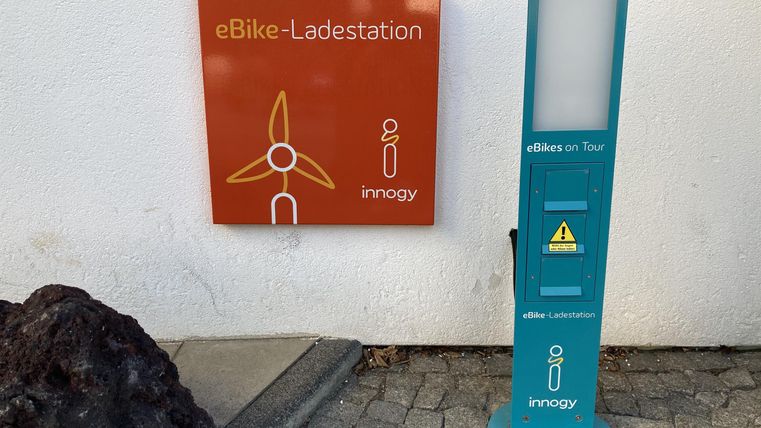 Eine eBike-Ladestation mit einem orangefarbenen Schild und einem blauen Ladegerät. Die Station gehört zu der Firma innogy und ist für umweltfreundliches Laden ausgelegt.
