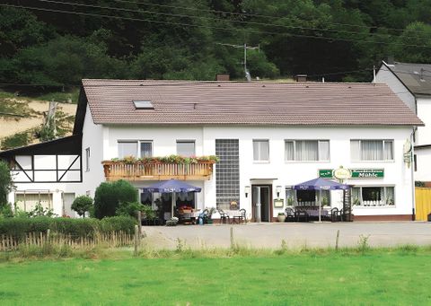 Ein zweigeschossiges Gebäude mit einem Balkon und Tischen im Freien. Die Umgebung ist grün und ländlich, ideal für einen ruhigen Aufenthalt.