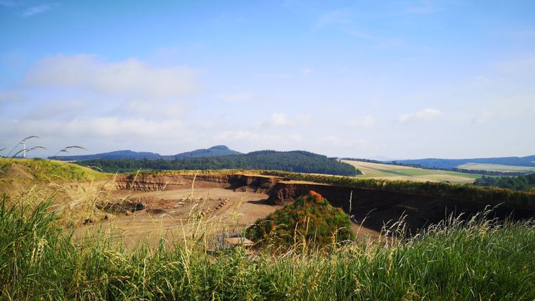 Landschaft mit Hügeln und Gräsern im Vordergrund, blauer Himmel.