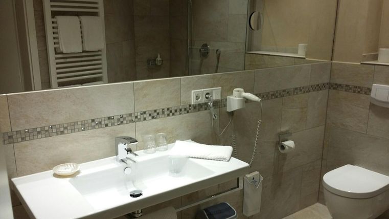 Ein modernes Badezimmer mit hellen Fliesen und einem Waschbecken. Handtücher und Toilettenartikel sind ordentlich angeordnet.