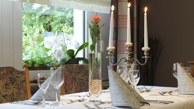 Ein elegant gedeckter Tisch mit Kerzenlicht und einem Blumenstrauß. Die Atmosphäre ist einladend und gemütlich.