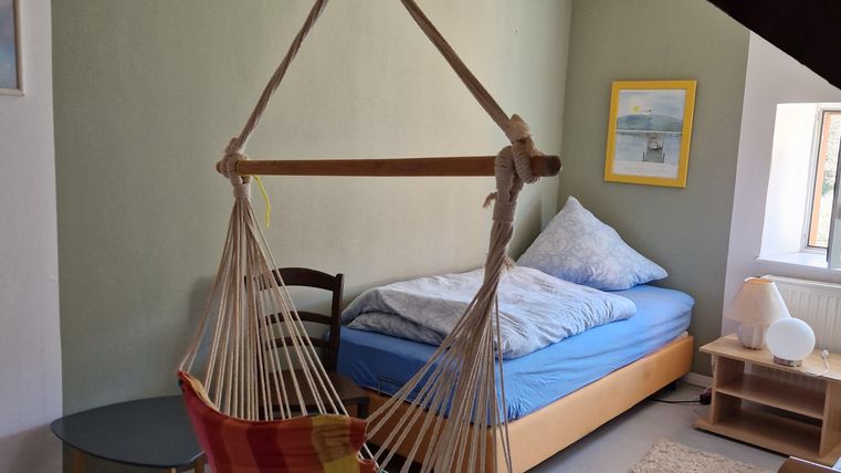 Ein gemütliches Zimmer mit einem hängenden Stuhl und einem Bett. Die Wände sind in sanften Farben gestrichen und es gibt einen kleinen Tisch.