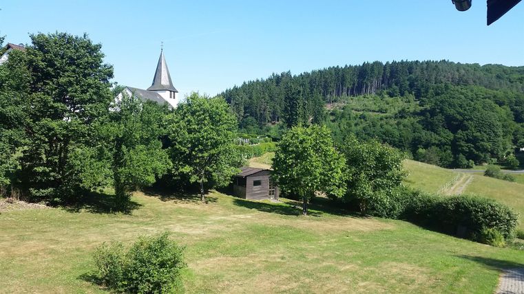 Eine ruhige Landschaft mit Bäumen und einer kleinen Hütte. Im Hintergrund steht eine Kirche und Wälder umgeben die Szene.