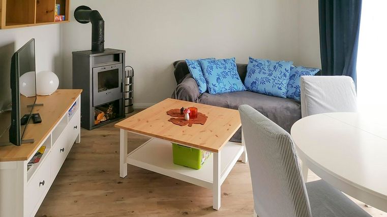 Ein gemütliches Wohnzimmer mit einer modernen Couch und blauen Kissen. Der Holzofen und der Tisch sind zentrale Elemente des Raumes.