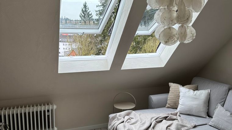 Ein gemütlicher Wohnraum mit einer modernen Couch und einem runden Tisch. Die großen Fenster lassen viel Tageslicht herein und bieten einen Blick ins Freie.