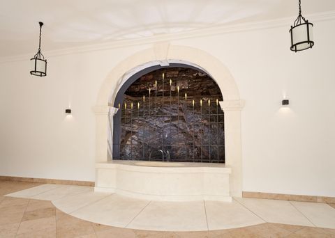 Eine elegante Wand mit einem Wasserbecken und einer dekorativen Steinwand. Sanfte Beleuchtung und architektonische Details sorgen für eine ruhige Atmosphäre.