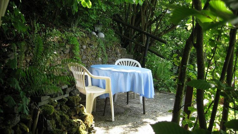 Ein gemütlicher Tisch mit blauer Tischdecke steht im Grünen. Umgeben von Pflanzen und Bäumen lädt die Ecke zum Entspannen ein.