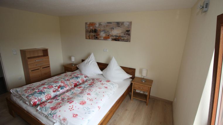 Ein gemütliches Schlafzimmer mit einem großen Bett und bunten Kissen. Neben dem Bett stehen Nachttische und es gibt eine harmonische Wanddekoration.
