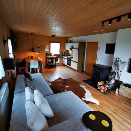 Ein gemütliches Wohnzimmer mit Holzdecken und einem großen Sofa. Die Einrichtung ist modern und einladend, mit einem Essbereich und einer Küche.