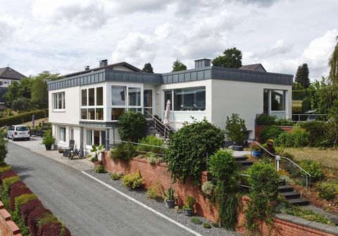 Ein modernes Haus mit großen Fenstern und einem gepflegten Garten. Die Umgebung ist grün und einladend.