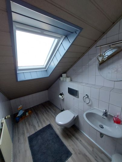 Ein helles Badezimmer mit Dachfenster und modernen Sanitäreinrichtungen. Die Wände sind gefliest und der Boden ist mit Holzoptik ausgelegt.