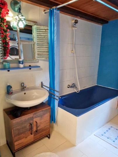 Ein Badezimmer mit einer Badewanne, einem Waschbecken und einer blauen Wand. Die Holzdecke verleiht dem Raum eine gemütliche Atmosphäre.