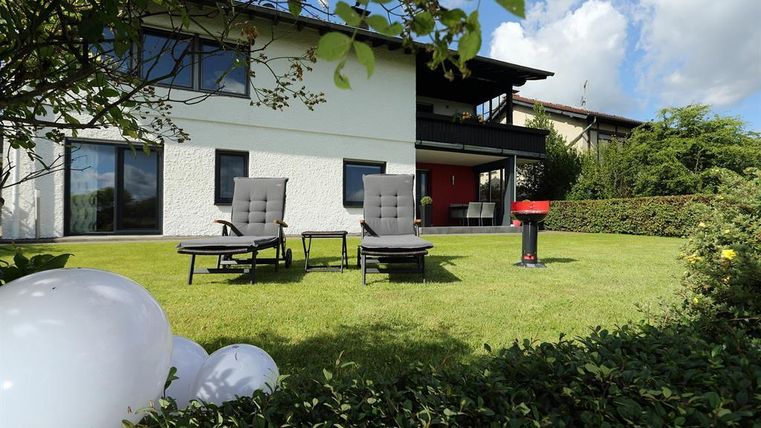 Ein gepflegter Garten mit zwei Liegestühlen und einem Grill. Das Gebäude im Hintergrund hat große Fenster und bietet einen einladenden Eindruck.
