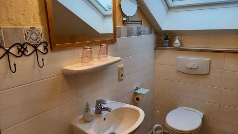 Ein kleines Badezimmer mit einem Waschbecken, einer Toilette und einem großen Fenster. Der Raum ist hell und modern eingerichtet.