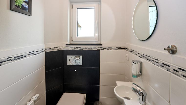 Ein modernes Badezimmer mit einer Toilette und einem kleinen Waschbecken. Ein Fenster und ein runder Spiegel sorgen für natürliches Licht und eine helle Atmosphäre.