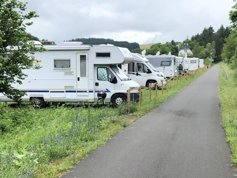 Mehrere Wohnmobile stehen entlang eines Weges, umgeben von grüner Vegetation. Die Stimmung ist ruhig und idyllisch.