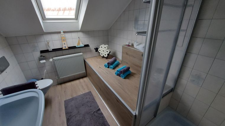 Ein modernes Badezimmer mit einem Fenster und Holzregalen. Die saubere Einrichtung umfasst eine Badewanne, eine Dusche und dekorierte Handtücher.