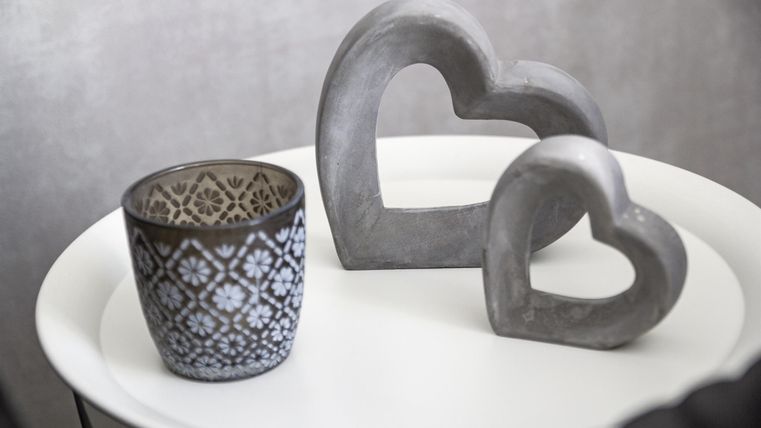 Ein stilvolles Deko-Arrangement mit zwei herzförmigen Skulpturen aus Beton und einem schönen, gemusterten Topf. Die Objekte stehen auf einem weißen Tisch und schaffen eine moderne Atmosphäre.