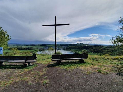 Ein schöner Aussichtspunkt mit einem großen Kreuz und Bänken. Im Hintergrund ist eine grüne Landschaft und ein ruhiger Fluss zu sehen.