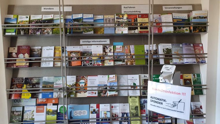 Ein Regal mit verschiedenen Informationsbroschüren zu verschiedenen Themen. Auf der Vorderseite steht ein Schild mit der Aufschrift "Automatischer Spender".