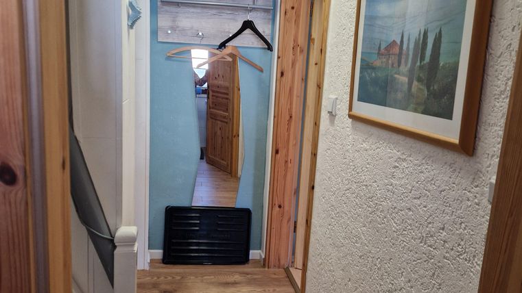 Ein heller Flur mit Holzfußboden und weißen Wänden. Im Hintergrund sind ein Bildrahmen und ein Kleiderständer zu sehen.