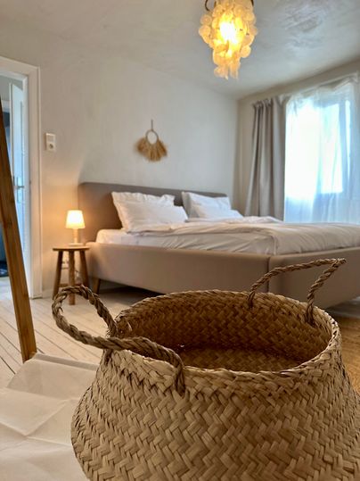 Ein gemütliches Schlafzimmer mit einem großen Bett und sanftem Licht. Im Vordergrund steht ein geflochtener Korb auf dem Boden.