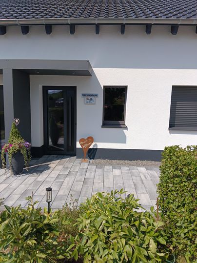 A modern house with an elegant front door. The entrance area is decorated with plants and has a paved path.