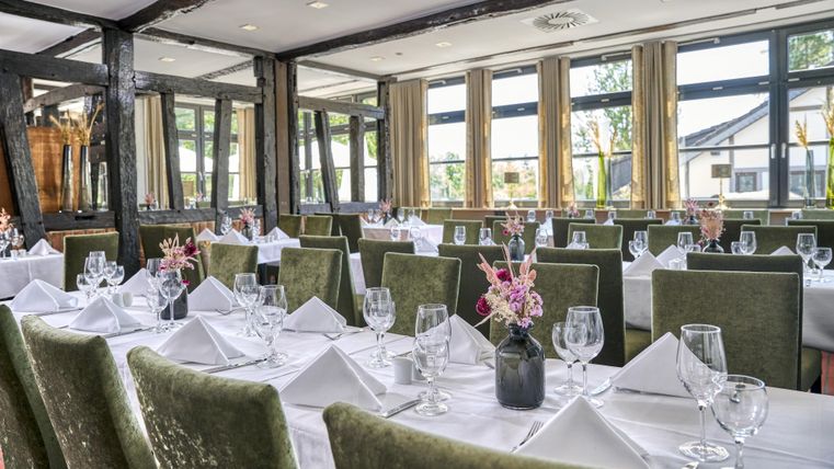 Ein elegantes Restaurant mit grünem Sitzbereich und schön gedeckten Tischen. Viele Fenster sorgen für viel natürliches Licht und eine einladende Atmosphäre.