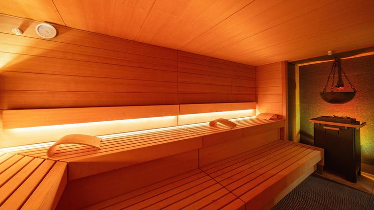 Eine gemütliche Sauna mit Holzbank und sanfter Beleuchtung. Im Hintergrund befindet sich ein Ofen für die Wärme.