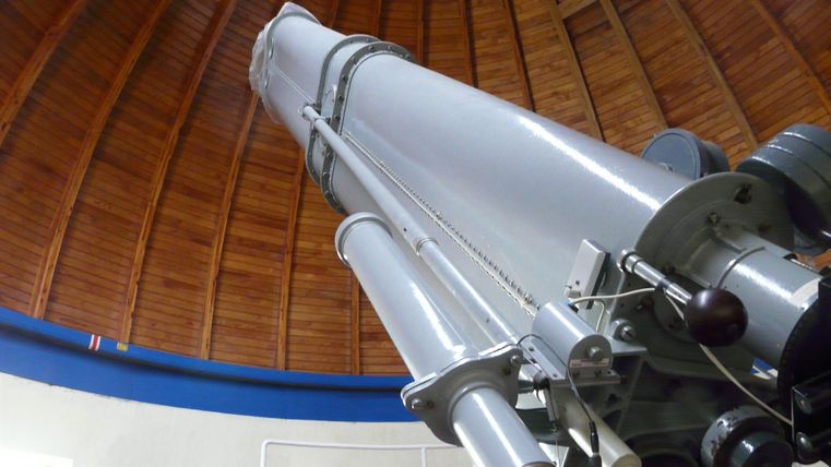 Ein großes Teleskop in einem Observatorium. Die Holzdecke ist sichtbar und verleiht dem Raum eine besondere Atmosphäre.