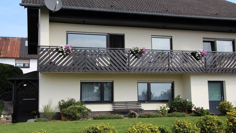 Ein gemütliches Haus mit einem Balkon, geschmückt mit Blumen. Der Garten ist gepflegt und grünt mit Sträuchern und Pflanzen.