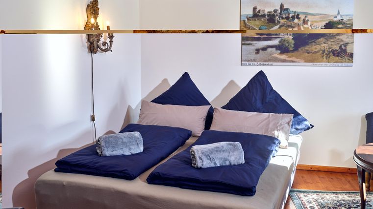 Ein gemütliches Schlafzimmer mit einem Doppelbett und blauen Kissen. An der Wand hängt ein Bild einer Landschaft.