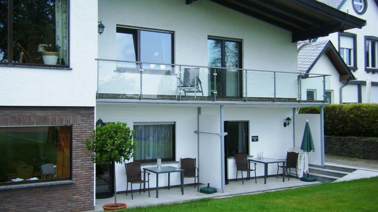 Ein modernes Gebäude mit einem Balkon und Terrassenmöbeln im Garten. Die Fassade ist hell gestrichen und von grünem Rasen umgeben.