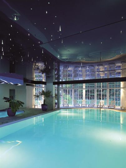 Ein eleganter Innenpool mit klarem, blauem Wasser. Die Decke ist mit funkelnden Lichtern geschmückt und große Fenster sorgen für viel Tageslicht.