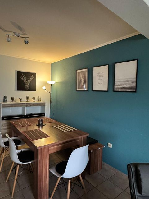 Ein modernes Esszimmer mit einem Holzstich-Tisch und weißen Stühlen. Die Wände sind in einem beruhigenden Blau gestrichen und es gibt dekorative Bilder.