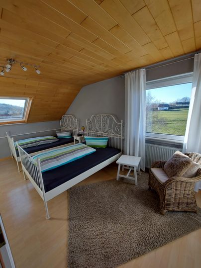 Ein gemütliches Schlafzimmer mit zwei Einzelbetten und modernen weißen Möbeln. Große Fenster bieten einen Blick auf die grüne Landschaft.