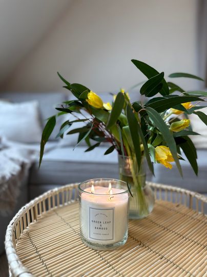 Eine gemütliche Tischdekoration mit einer Kerze und einem Blumenstrauß. Die Blumen sind gelb und grün, während die Kerze sanft leuchtet.
