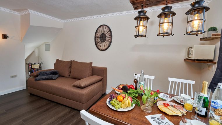 Ein gemütliches Wohn- und Esszimmer mit einem Sofa und einem Esstisch. Auf dem Tisch sind frisches Obst und Getränke angerichtet.
