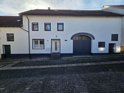 Ein modernes Haus mit einer weißen Fassade und mehreren Fenstern. Die Eingangstür ist gut sichtbar und ein großes Tor ist ebenfalls vorhanden.