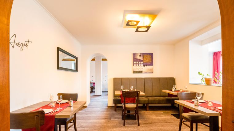 Ein gemütliches Restaurant mit Holzstühlen und Tischen. Die Wände sind hell und freundlich, und es gibt eine elegante Beleuchtung.