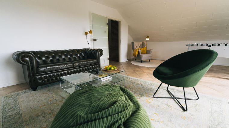Ein modernes Wohnzimmer mit einem eleganten, schwarzen Sofa und einem grünen Sessel. Der Raum hat einen hellen und freundlichen Charakter mit einem neutralen Farbton.