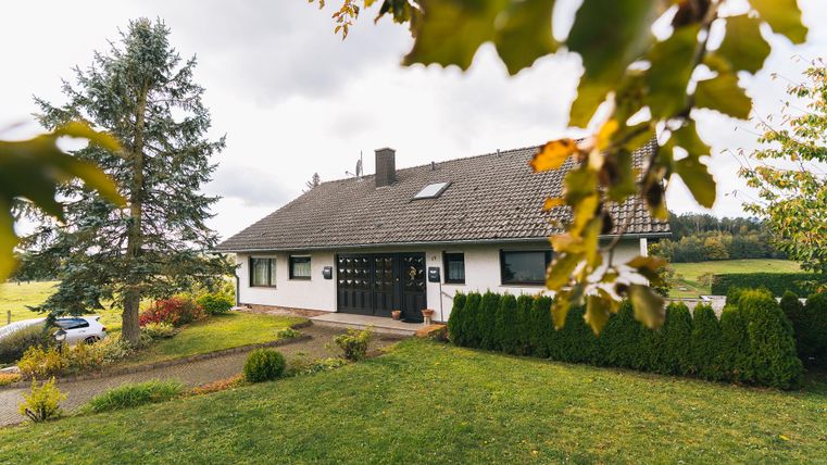 Ein schönes Einfamilienhaus umgeben von Grün und Bäumen. Die Fassade ist hell mit einer dunklen Eingangstür.