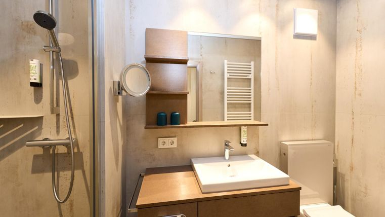 Ein modernes Badezimmer mit einer Dusche und einem Waschbecken aus Holz. Es gibt einen großen Spiegel und eine praktische Ablagefläche.