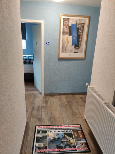 Ein heller Flur mit blauen Wänden und einem Kunstwerk an der Wand. Auf dem Boden liegt ein auffälliger Teppich.