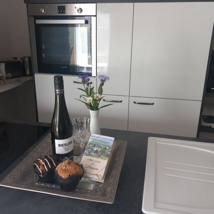 A modern kitchen with a tray that displays a bottle of wine, glasses, muffins, and fresh flowers. The space is bright and inviting.